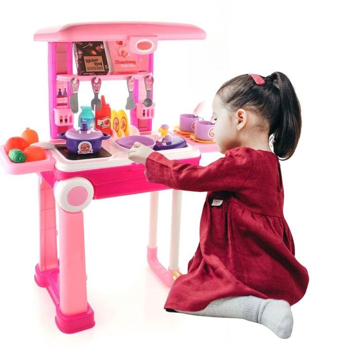 Child playing with a pink kids kitchen play set with lights featuring utensils and toy food items