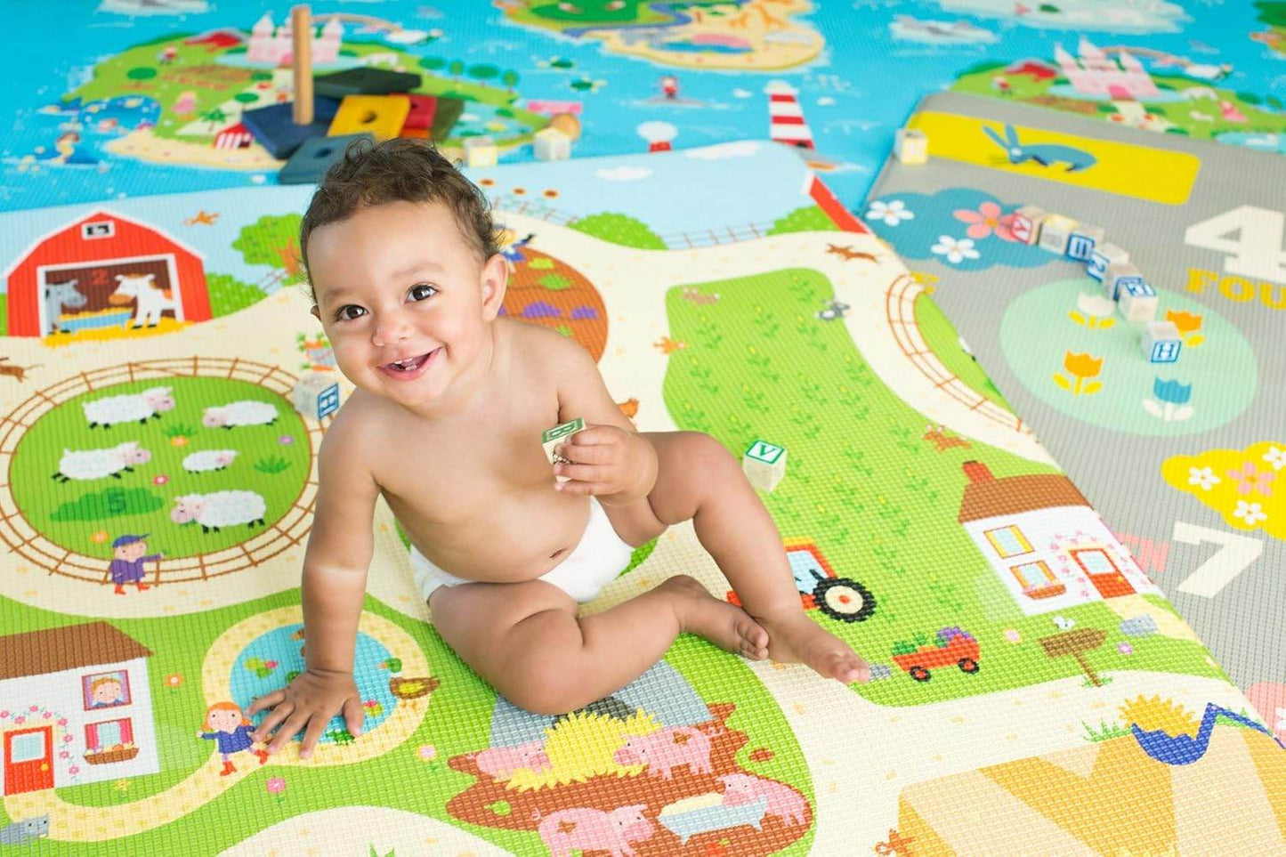 Baby sitting and playing on Unimates farm themed baby mat with colorful animal and farm illustrations