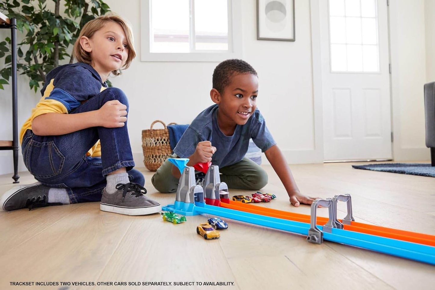 Two kids playing with Hot Wheels Action Dual Loop Dash race track set on a wooden floor