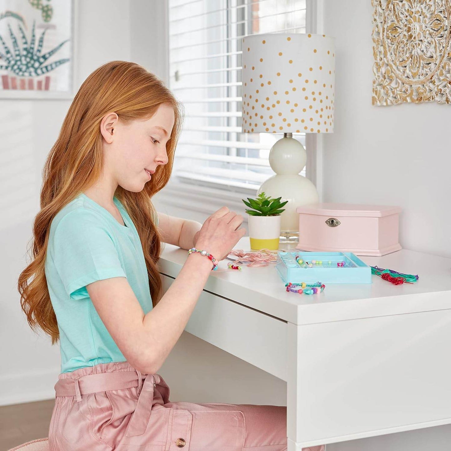 Young girl making bracelets using a DIY charm bracelet kit for kids at a white desk