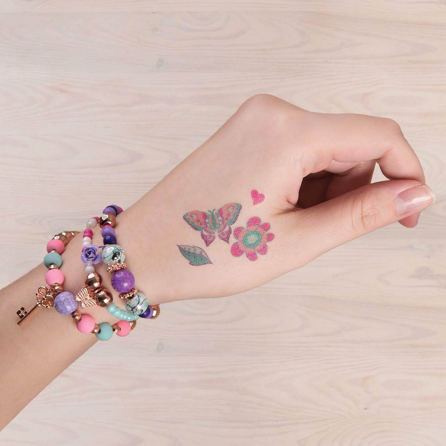Hand wearing colorful beaded bracelets with butterfly and flower tattoos showcasing DIY jewelry kit for girls