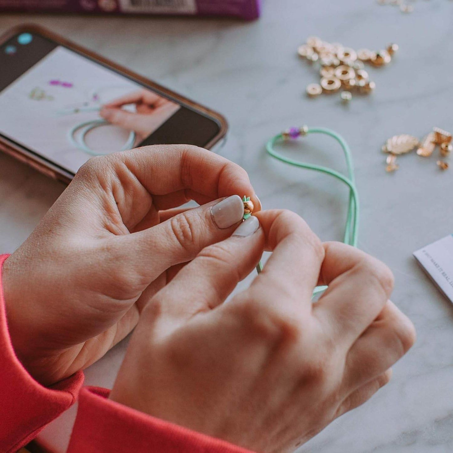Hands assembling jewelry with kids jewelry making set 112 pieces and smartphone tutorial on table