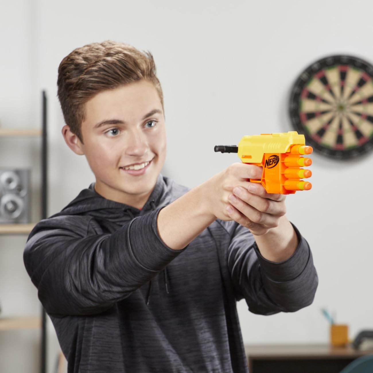 Teen boy holding Hasbro Nerf Alpha Strike set yellow toy gun with multiple dart barrels indoors
