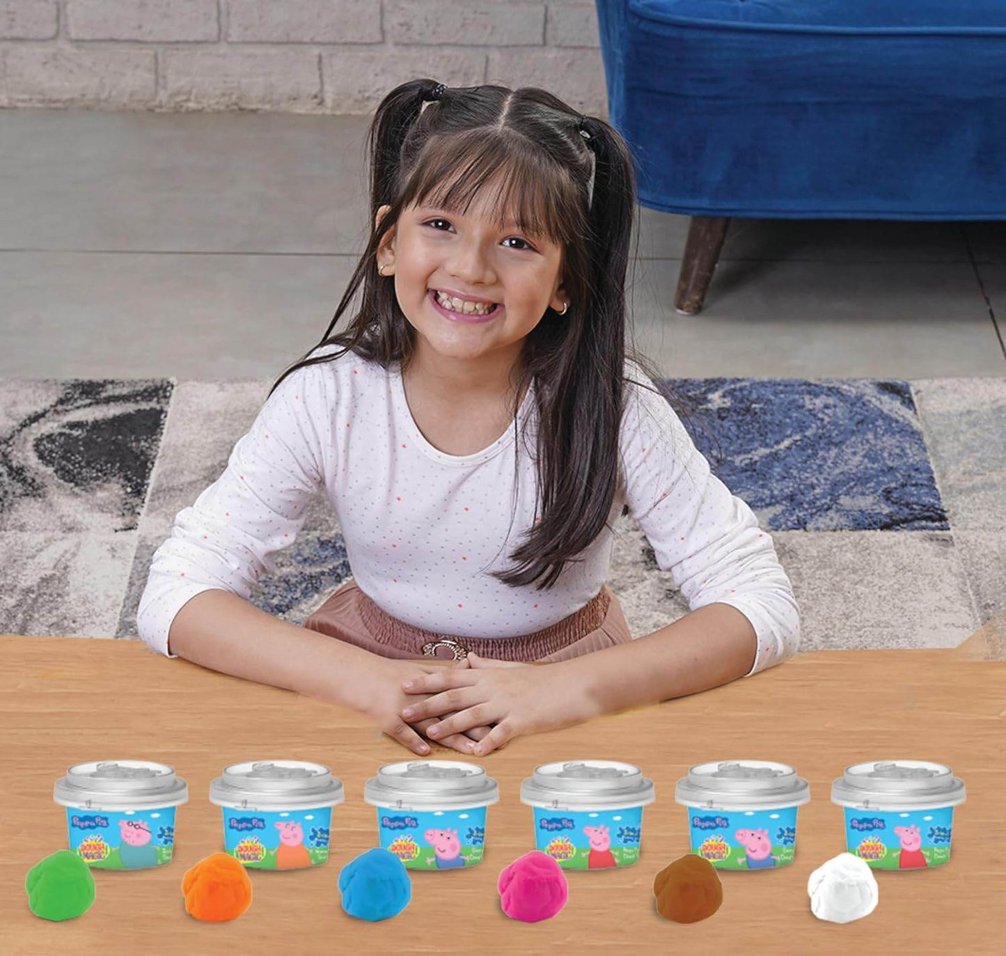Smiling girl with Peppa Pig dough tubs set in various colors on wooden table indoors