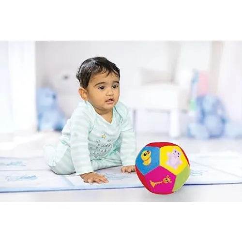 Infant playing with a colorful softball for infants on a soft mat indoors