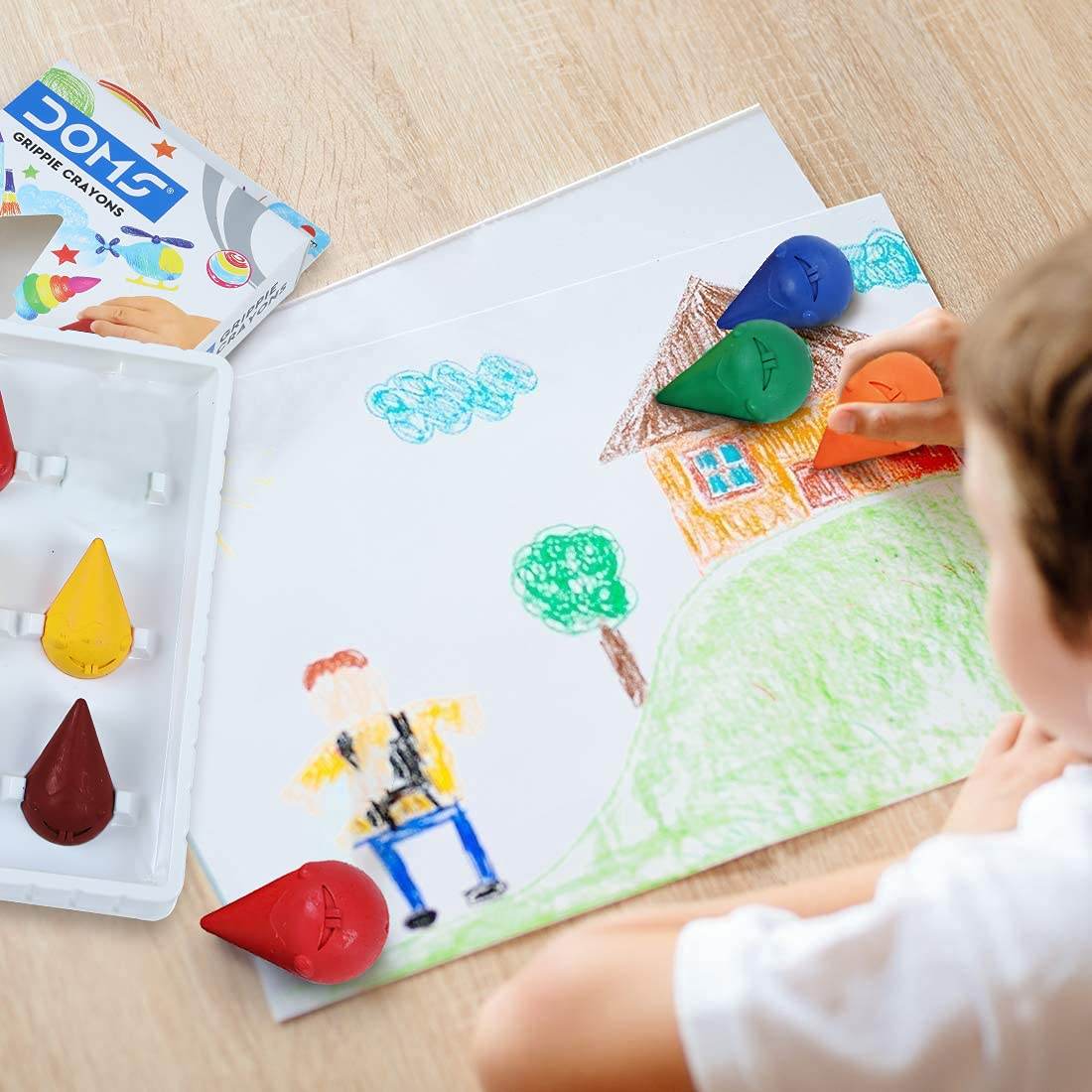Child using Doms grippie crayons for toddlers to color a house and tree drawing on paper