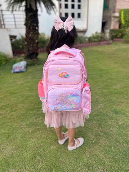 Young girl wearing a pink large capacity unicorn bag for school standing on grass outside