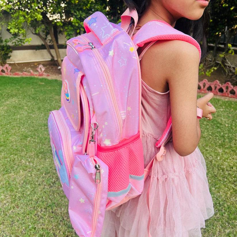 Girl wearing a large capacity unicorn bag for school in pink with star and rainbow designs outdoors