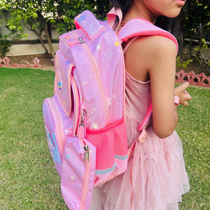 Girl wearing a large capacity unicorn bag for school in pink with star and rainbow designs outdoors