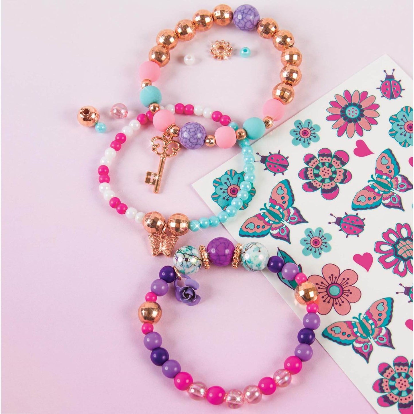 Colorful DIY jewelry kit for girls with beaded bracelets and decorative stickers on a pink background