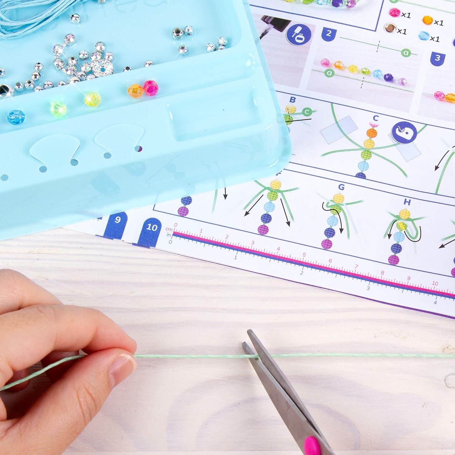 Hands cutting thread with scissors next to beads and instructions for rainbow bling bracelet kit