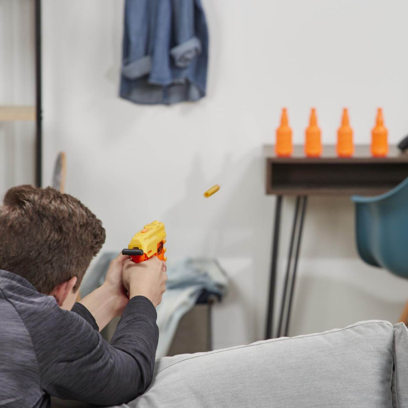 Person aiming and firing a yellow toy gun from the Nerf Alpha Strike set indoors at orange targets