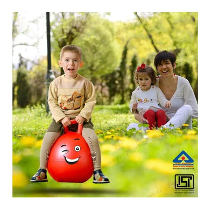 Young boy playing outdoors on a red rubber kangaroo hopping ball for kids with woman and child in background