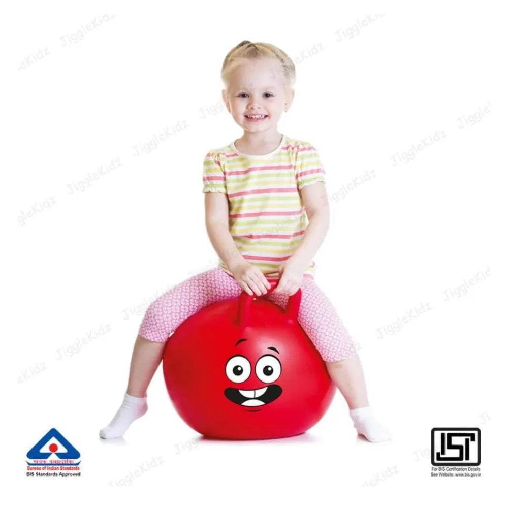 Child sitting on a red rubber kangaroo hopping ball for kids with a smiling face design